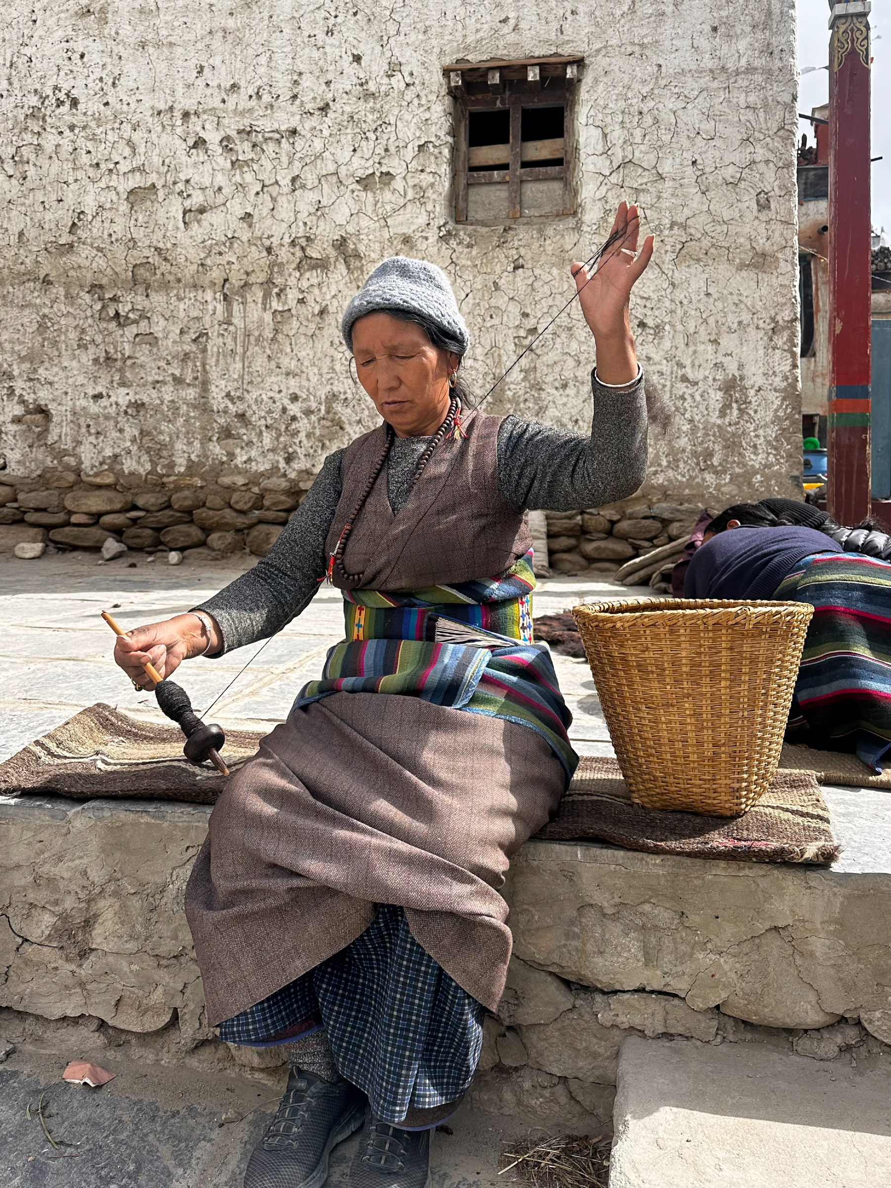An elderly woman in Lo Manthang demonstrates the traditional art of weaving leg warmers from yak wool in Lo Manthang, the walled capital of Upper Mustang.

Lo Manthang sits in a Himalayan rain shadow shaped by wind-swept plateaus, deep eroded canyons and minimal rainfall. Founded by Ame Pal and encircled by mud-brick walls built to defend against bandits and rival kingdoms, it was once an independent kingdom. Its extreme isolation has helped preserve Tibetan Buddhist culture, language, customs and daily life.

Yet that same isolation has become a growing challenge. With the closure of Tibetan trade routes around 1959, the community shifted from a thriving trade hub to a fragile agro-pastoral economy. Today, springs are drying, pastures are shrinking, and snow leopards - driven by a shrinking prey base - increasingly descend into villages to prey on livestock, creating both economic and social strain.

The woman's hands, deftly working yak wool into a traditional garment, represent something larger: a living thread connecting Lo Manthang's people to their heritage. Supporting indigenous crafts such as weaving, beading and painting offers not only a potential option for sustainable livelihoods, but a means of cultural preservation, making tradition a source of both pride and prosperity for future generations.